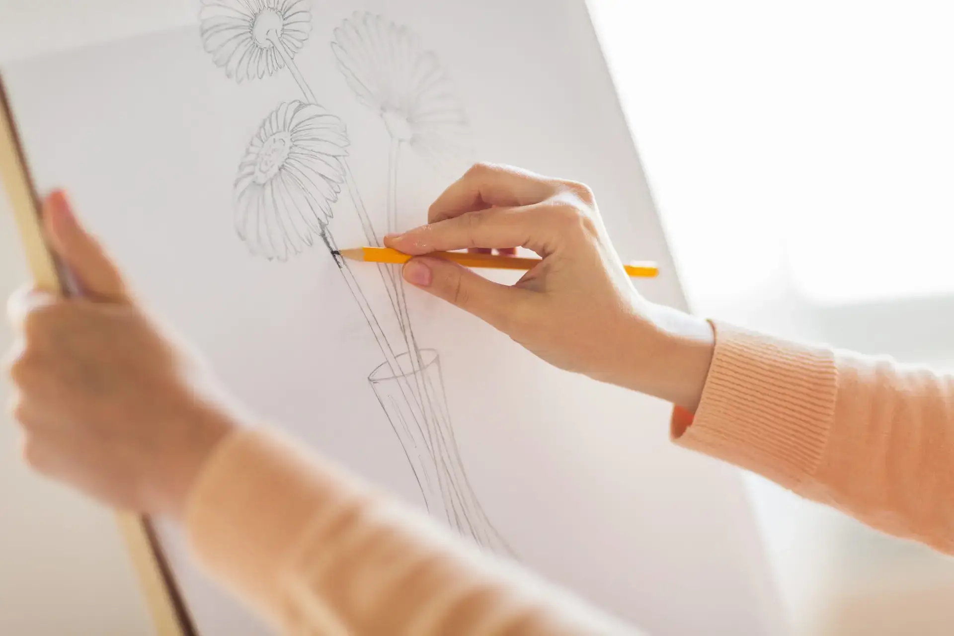 art, creativity and people concept - artist hands with graphite pencil drawing still life picture of flower in vase on paper at studio